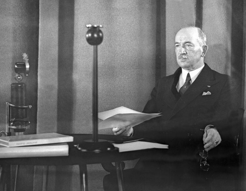 Prezident Edvard Beneš sedí u rozhlasového mikrofonu s papíry v ruce